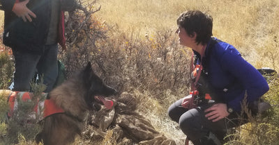 A woman crouches down in front of her search and rescue dog. 